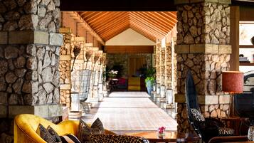 A spacious lobby with a stone wall, wooden ceiling beams, and a central seating area with a yellow sofa and leopard print chairs.