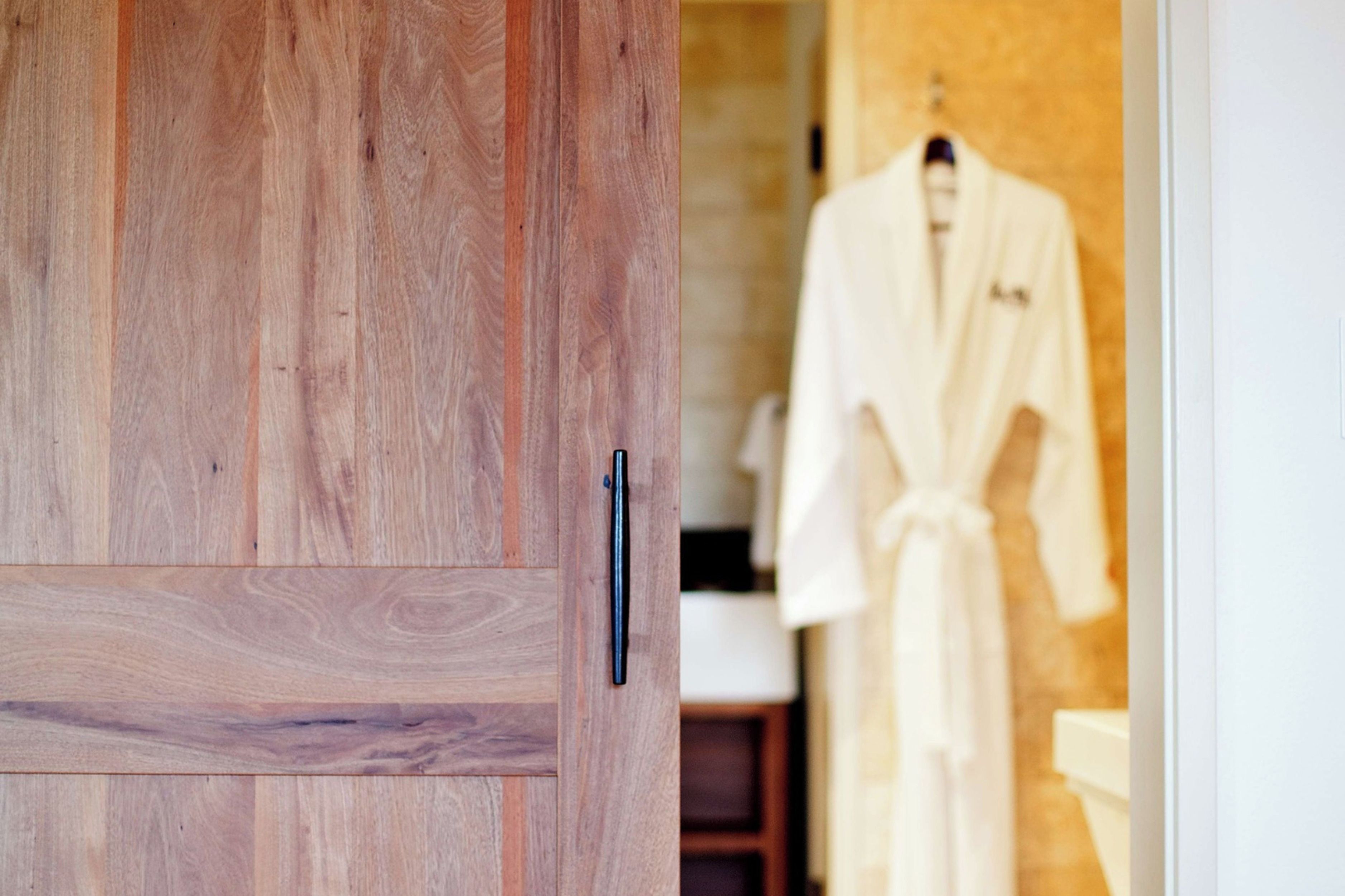 Une porte en bois avec une poignée noire, qui donne sur une pièce où est accrochée une robe blanche au mur.