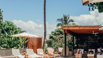 A poolside area with lounge chairs, a palm tree, and a wooden pergola.