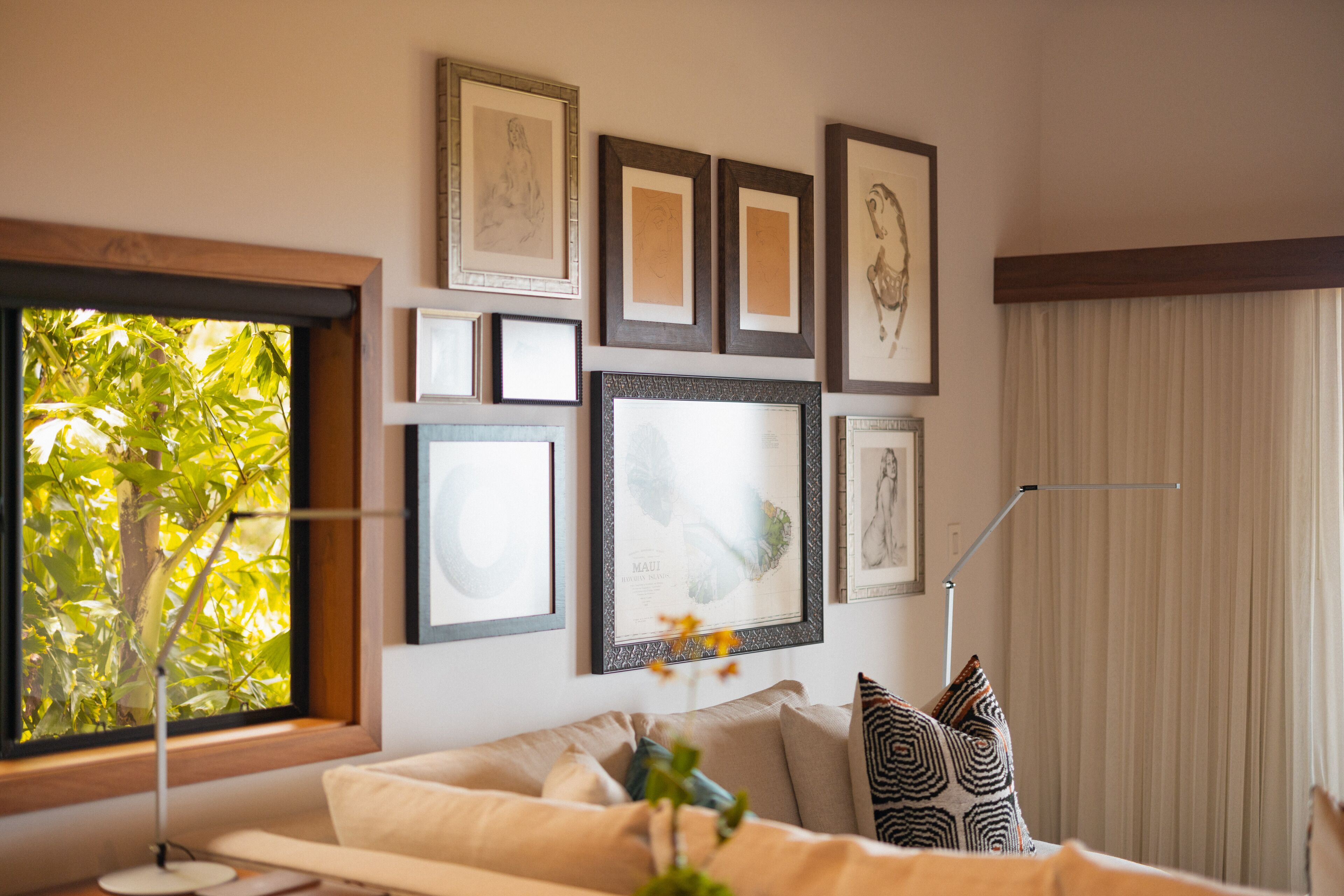 Een woonkamer met een groot raam, een bank en diverse ingelijste foto's aan de muur.