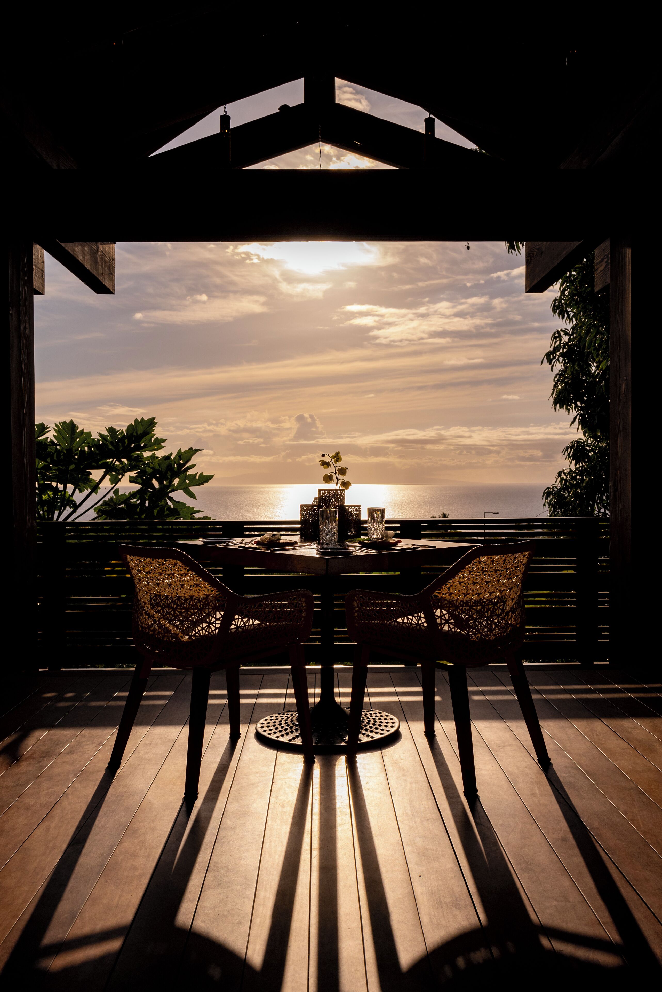 Een houten terras met een tafel en stoelen, gericht op een zonsondergang boven de oceaan.