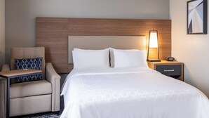 Una habitación de hotel con una cama, una mesita de noche, una lámpara, una silla y un almohadón.