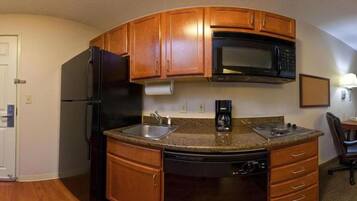 A compact kitchen with wooden cabinets, a black refrigerator, a microwave, a coffee maker, and a dishwasher.
