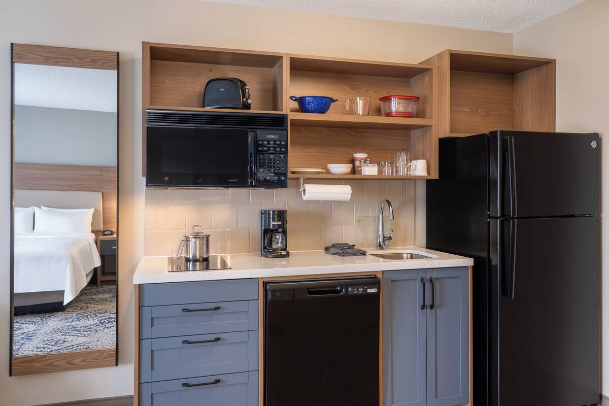 A compact kitchen with a microwave, coffee maker, and a black refrigerator.