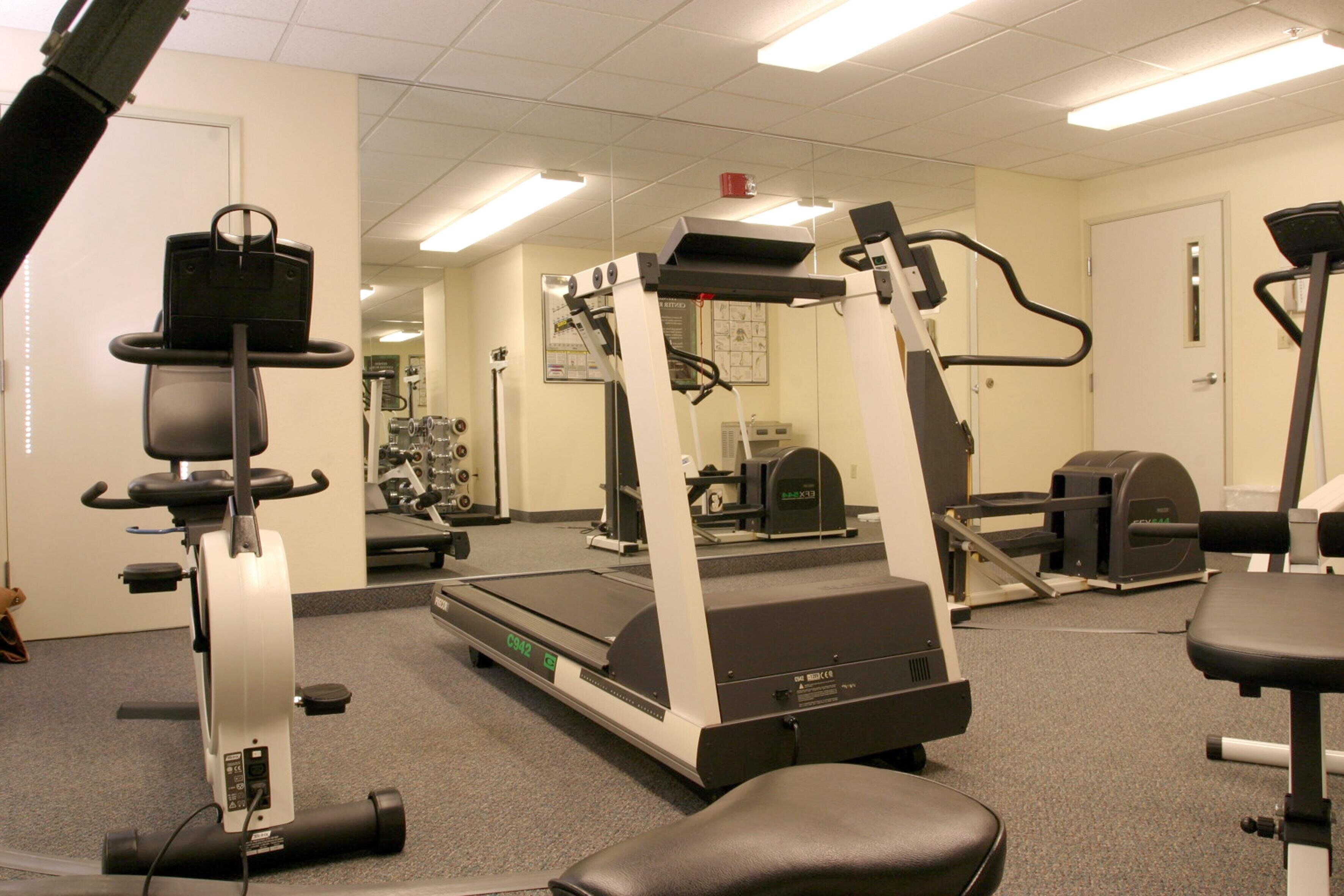 A gym with cardio machines, weight stations, and mirrors on the walls.