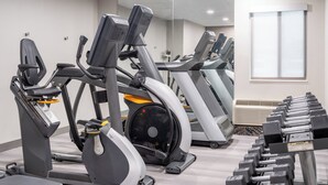Un gimnasio con varias máquinas de ejercicio, incluyendo cintas de correr y elípticas, dispuestas en filas.