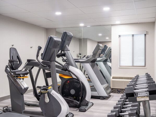 Ein Fitnessstudio mit mehreren Trainingsgeräten, darunter Laufbänder und Crosstrainer, die in Reihen angeordnet sind.