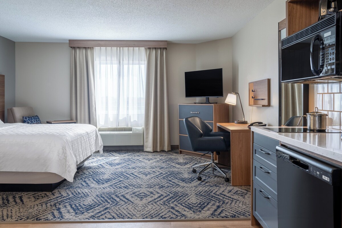 Ein Hotelzimmer mit Bett, Schreibtisch, Stuhl, Fernseher, Mikrowelle und Geschirrspüler.