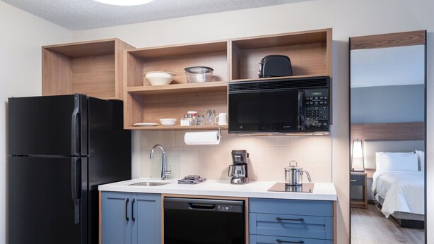 Eine kompakte Küche mit einem schwarzen Kühlschrank, einer Mikrowelle, einer Kaffeemaschine und einem Geschirrspüler.