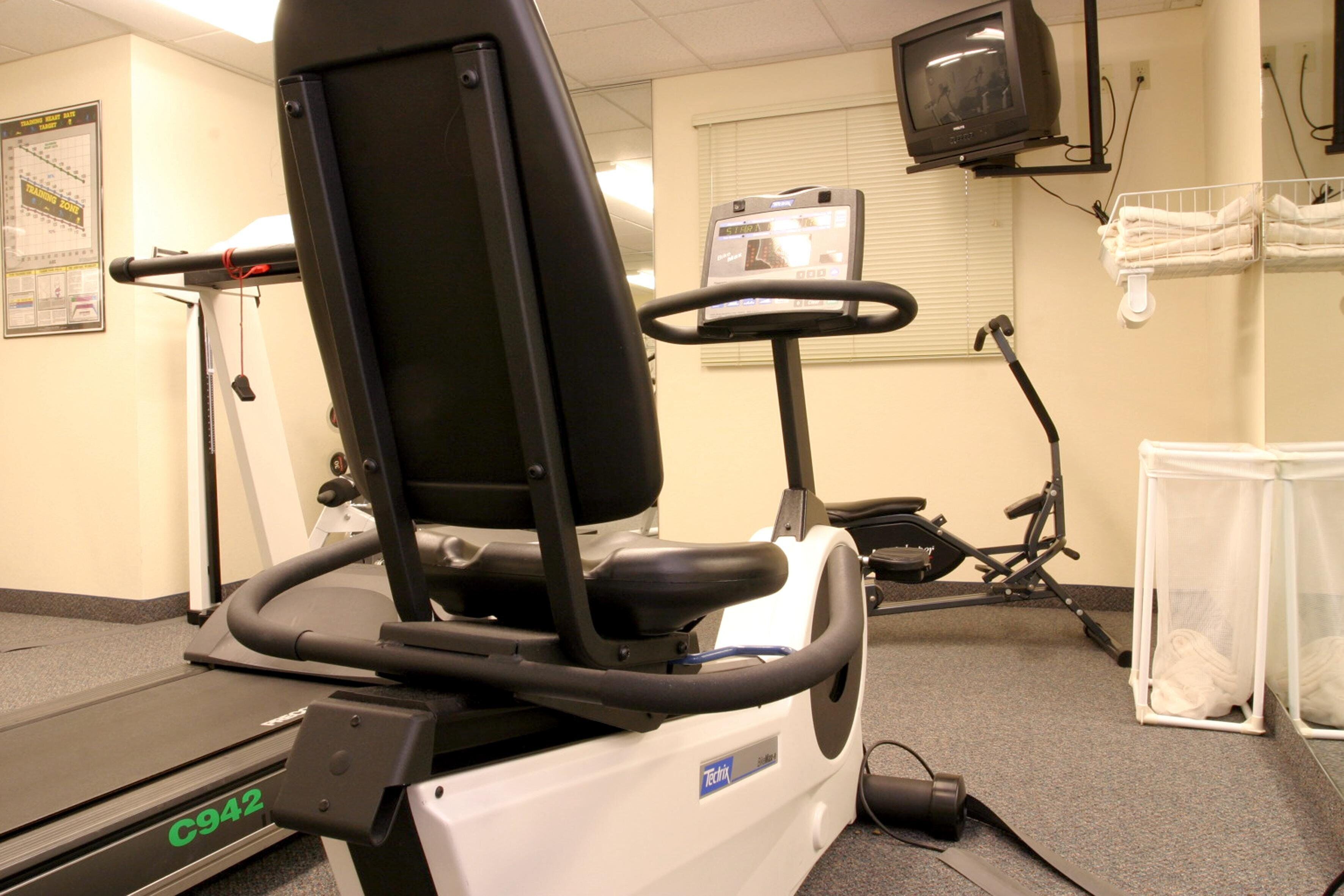 A stationary bike with a digital display, a treadmill, and a television mounted on the wall.