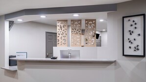 Un mostrador de recepción de diseño moderno, una obra de arte enmarcada en la pared y una puerta al fondo.