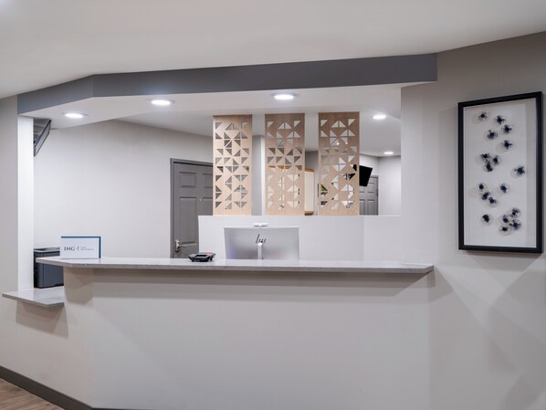 Un mostrador de recepción de diseño moderno, una obra de arte enmarcada en la pared y una puerta al fondo.