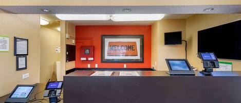 A reception desk with a 'WELCOME' sign, a TV, and a digital payment terminal.