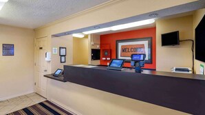 A reception desk with a 'WELCOME' sign, a computer, a phone, and a TV. - Extended Stay America Select Suites Tampa North Airport (Tampa)