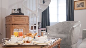 Una bandeja de desayuno con huevos, tostadas y jugo sobre una mesa de madera en una habitación con un sillón gris y una escalera de caracol al fondo.