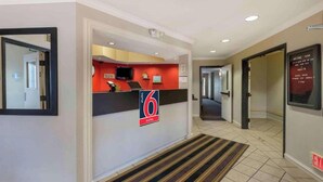 Zona de recepción de un hotel con mostrador, señalización que indica 6 suites, un reloj y un cartel que dice 'Welcome Home'.