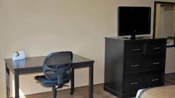 A hotel room with a desk, chair, television, and a dresser.