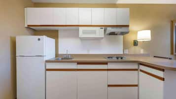 Cocina compacta con armarios blancos, microondas, refrigerador, lavamanos y una lámpara de pared.