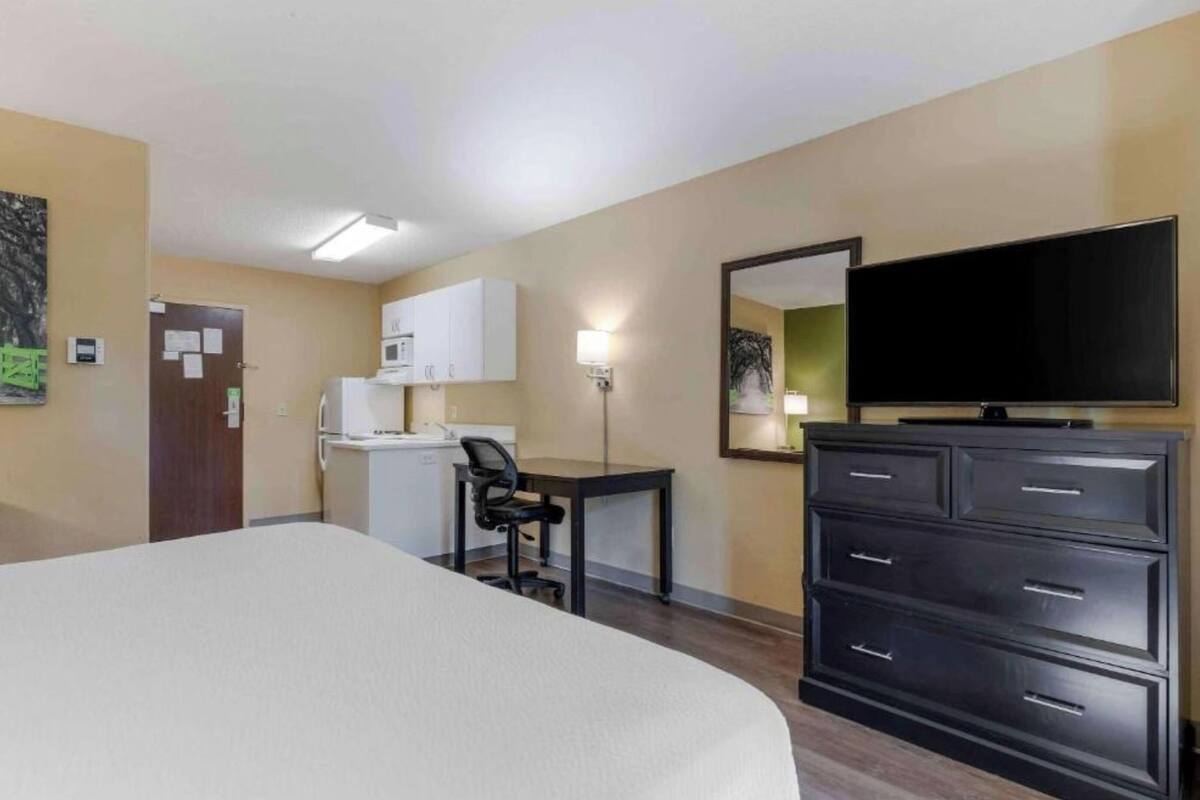 Une chambre d’hôtel équipée d’un lit, d’un bureau avec une chaise, d’un téléviseur à écran plat, d’une commode et d’un four à micro-ondes.