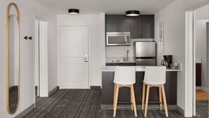 Een kleine keuken met een magnetron, koelkast en barstoelen.