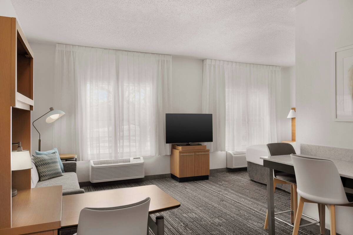 A modern hotel room with a flat-screen TV, a sofa, a dining table, and a chair.