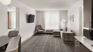 Een moderne hotelkamer met een flatscreen televisie, een zithoek met een tafel en stoelen, een bank, een klein rond tafeltje en een kitchenette.