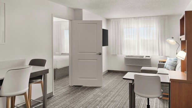 Een hotelkamer met een bed, een bureau, een stoel, een tafel, een lamp en een raam met gordijnen.