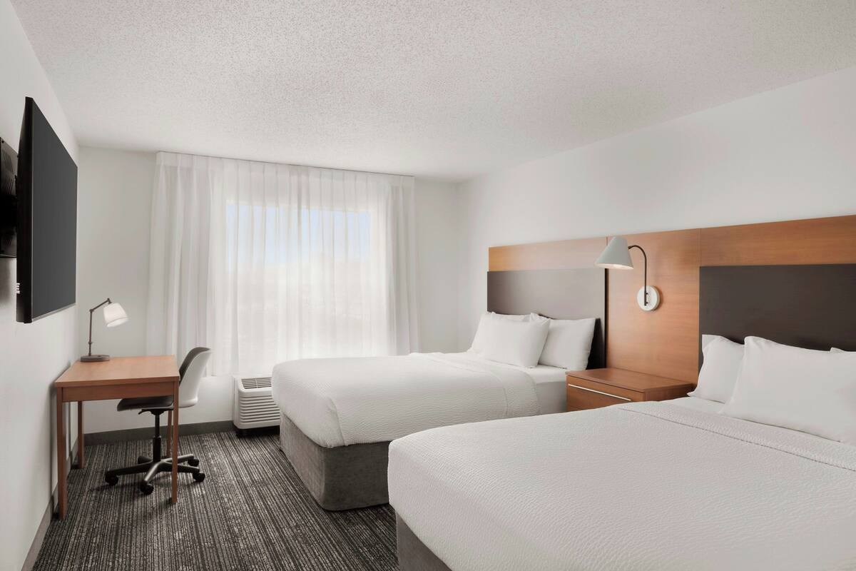 A hotel room with two beds, a desk, a chair, a TV, and a window with curtains.
