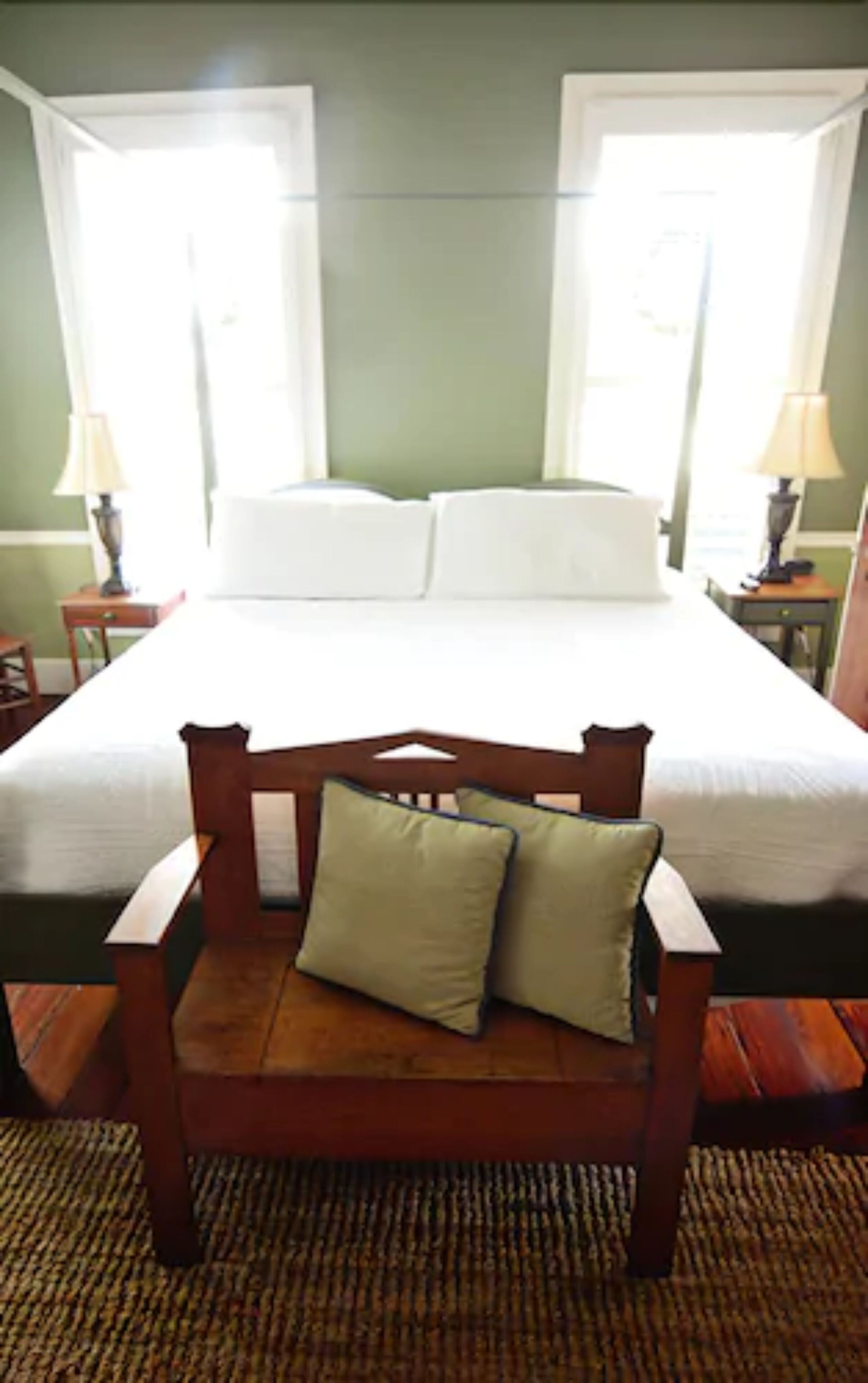 A bedroom with a large bed, two bedside tables, and a wooden chair with cushions.