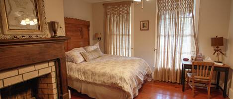 A bedroom with a wooden bed, a fireplace, a ceiling fan, and a desk with a chair.