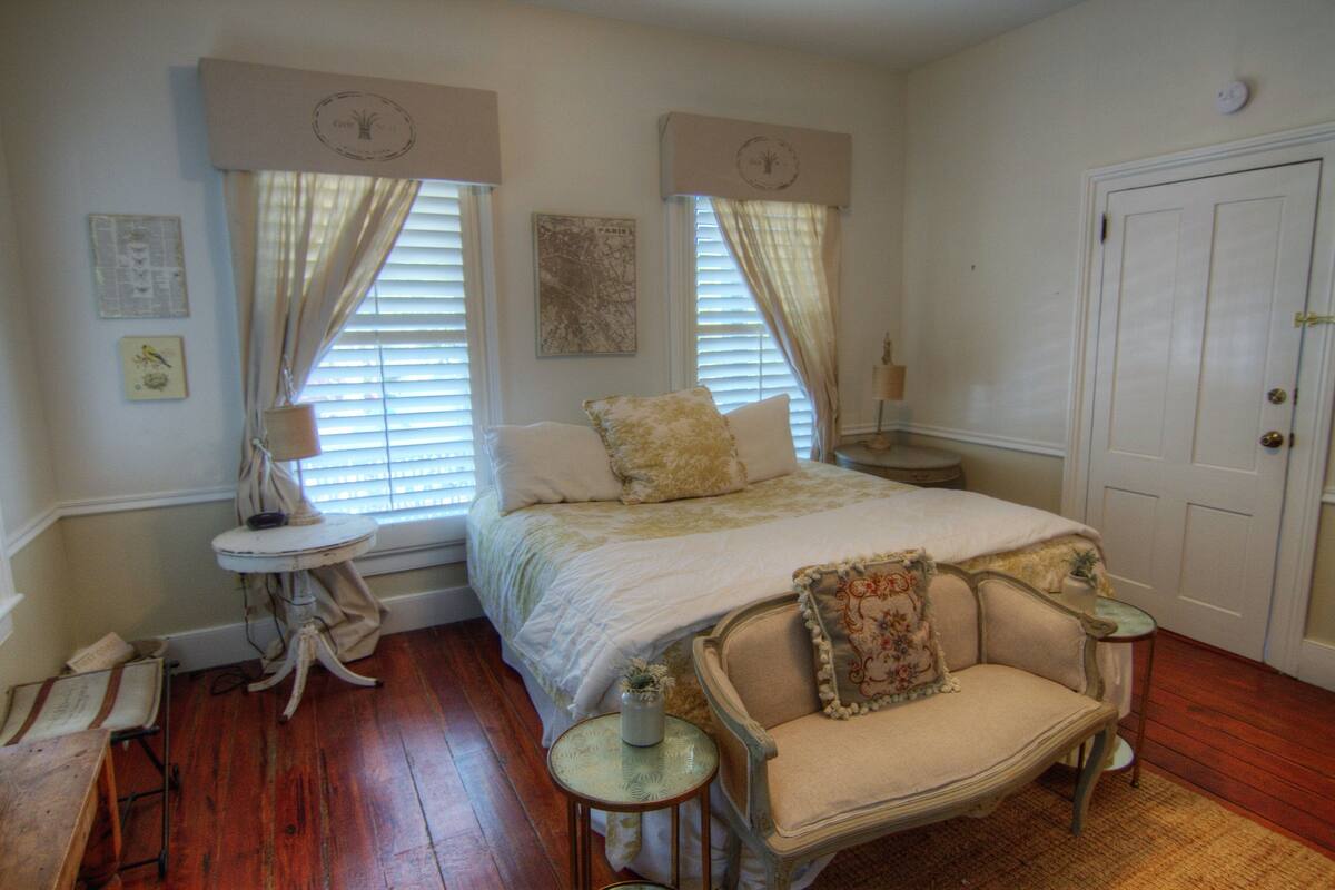 A bedroom with a bed, a chair, a small table, and a door.