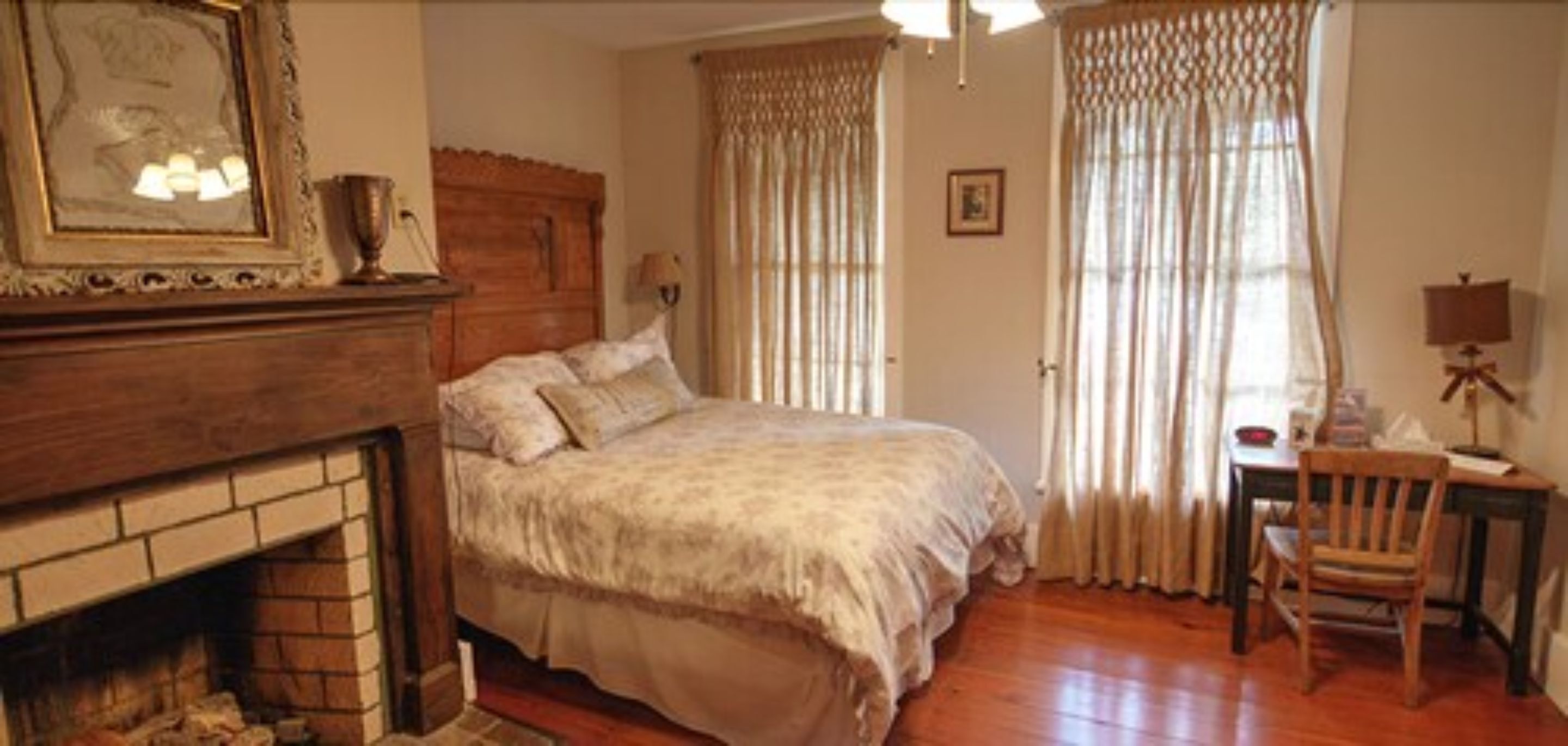 A bedroom with a wooden bed, a fireplace, a desk with a chair, and curtains.