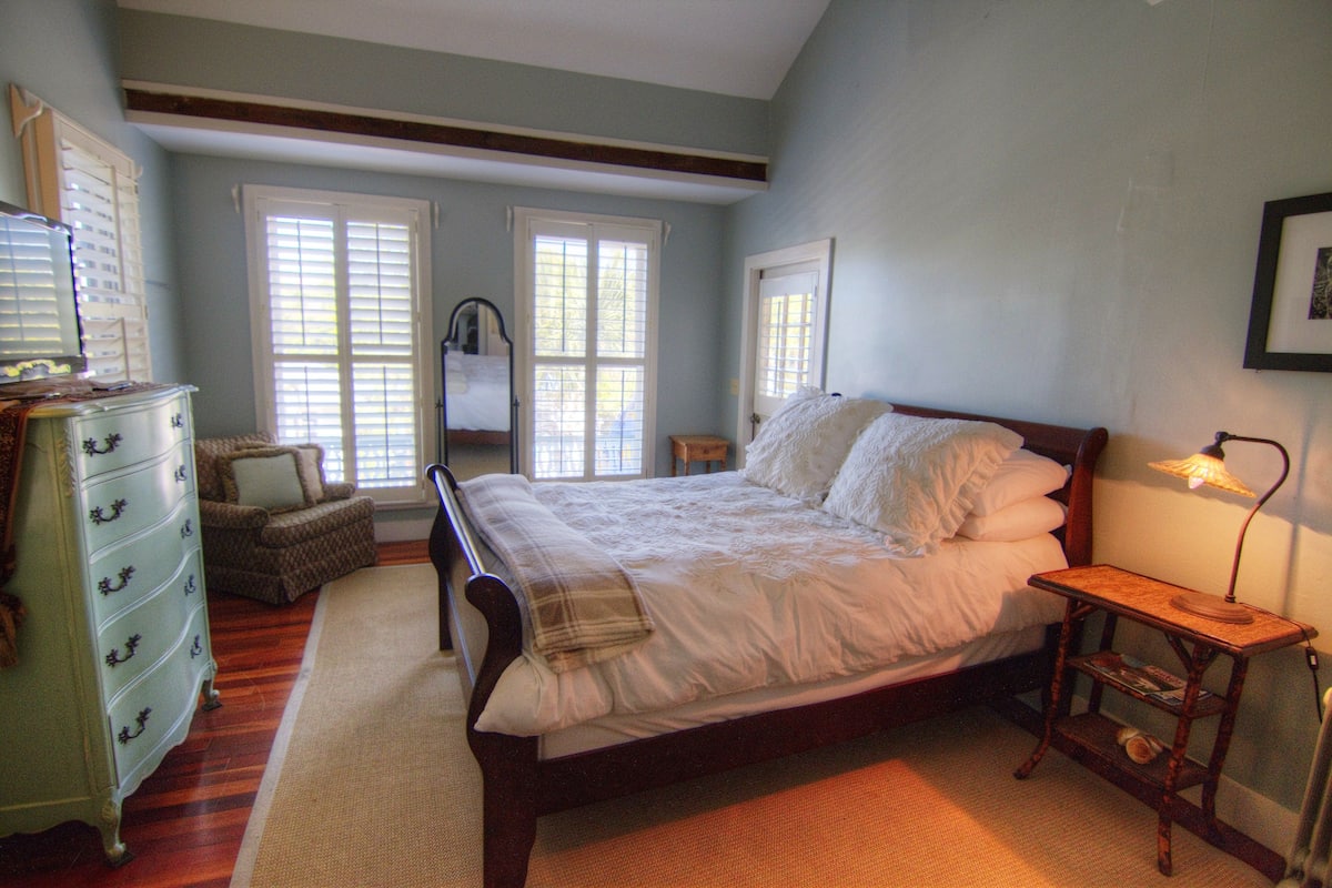 A bedroom with a large bed, dresser, and a small table with a lamp.