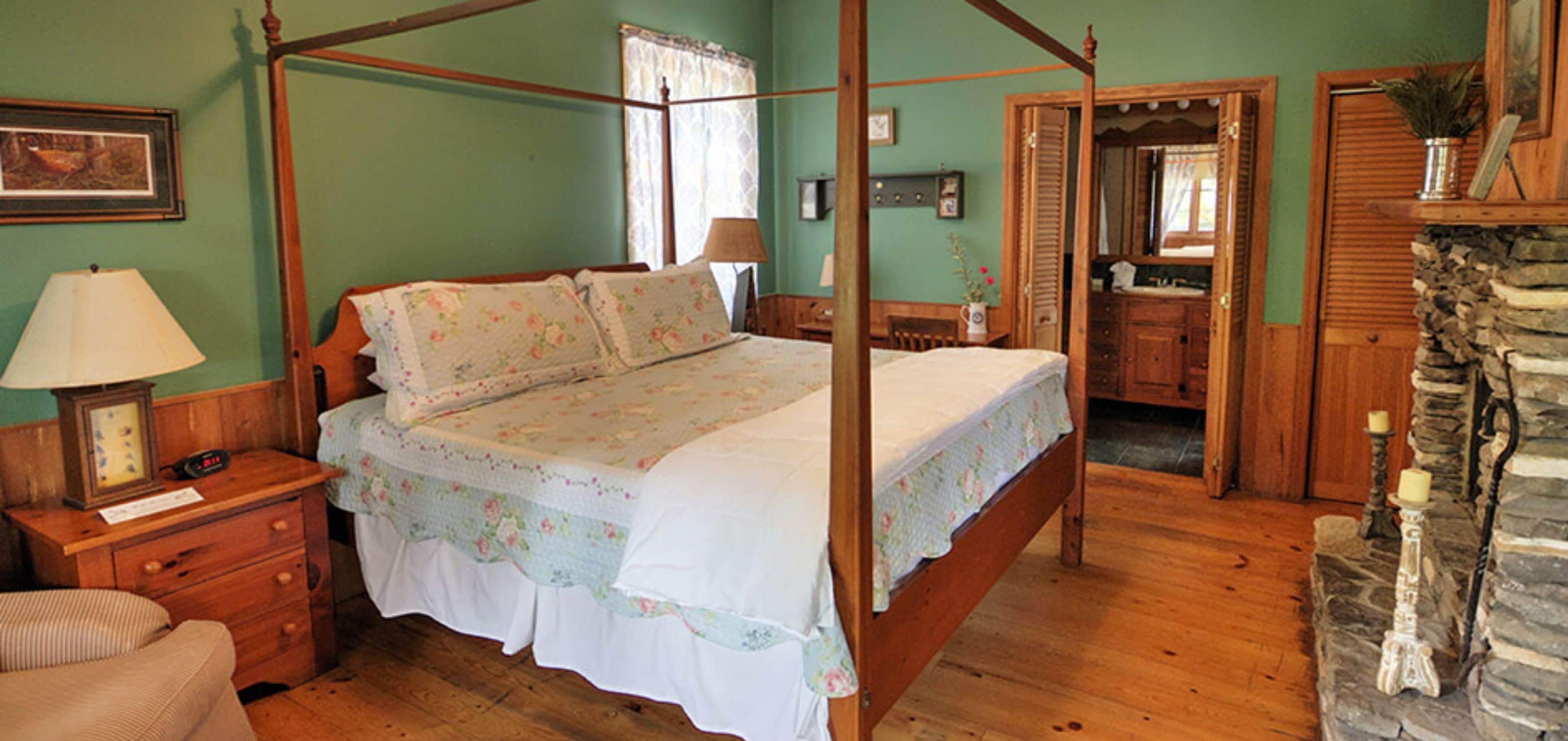 A four-poster bed with floral bedding, a wooden nightstand with a lamp, a dresser, and a stone fireplace.
