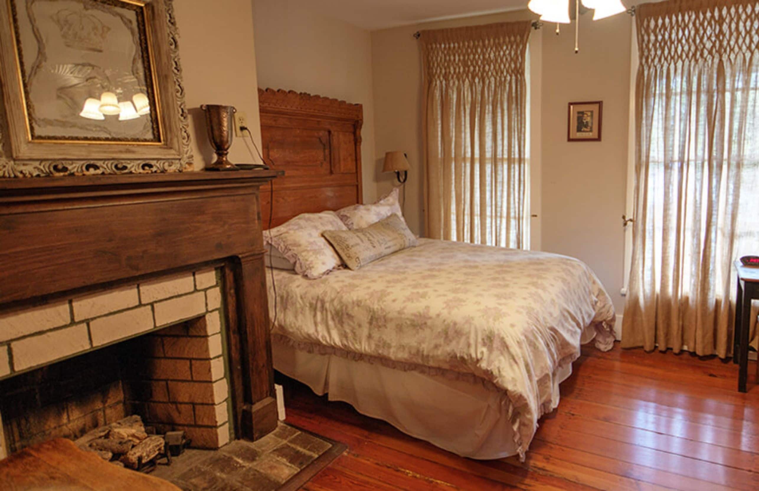 A bedroom with a fireplace, a bed, and a window with curtains.