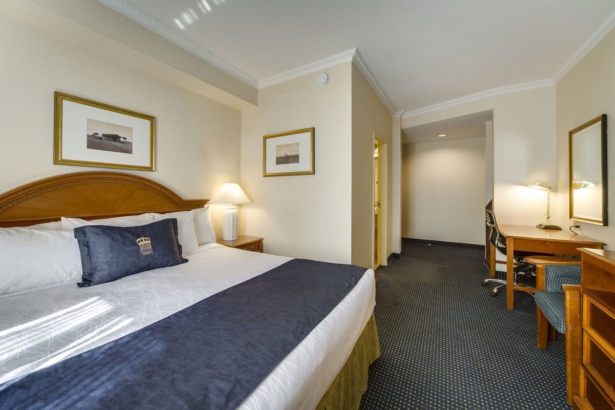 A hotel room with a bed, a desk, a chair, a lamp, and a mirror.