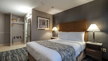 Habitación de hotel con una cama grande, dos mesitas de noche con lámparas, un cabecero de madera, un cuadro enmarcado en la pared y un perchero.