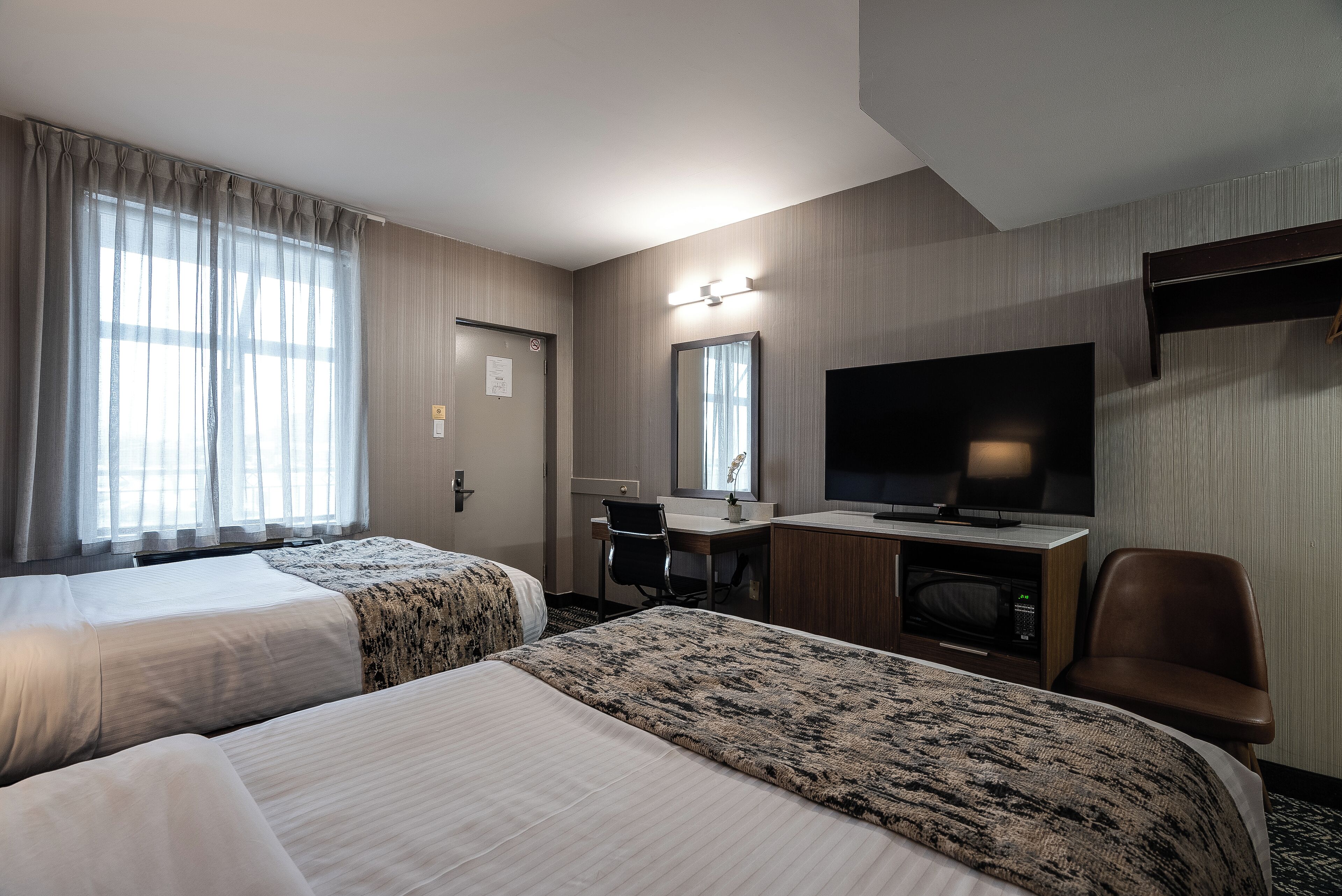 A hotel room with two beds, a desk, a TV, and a chair.