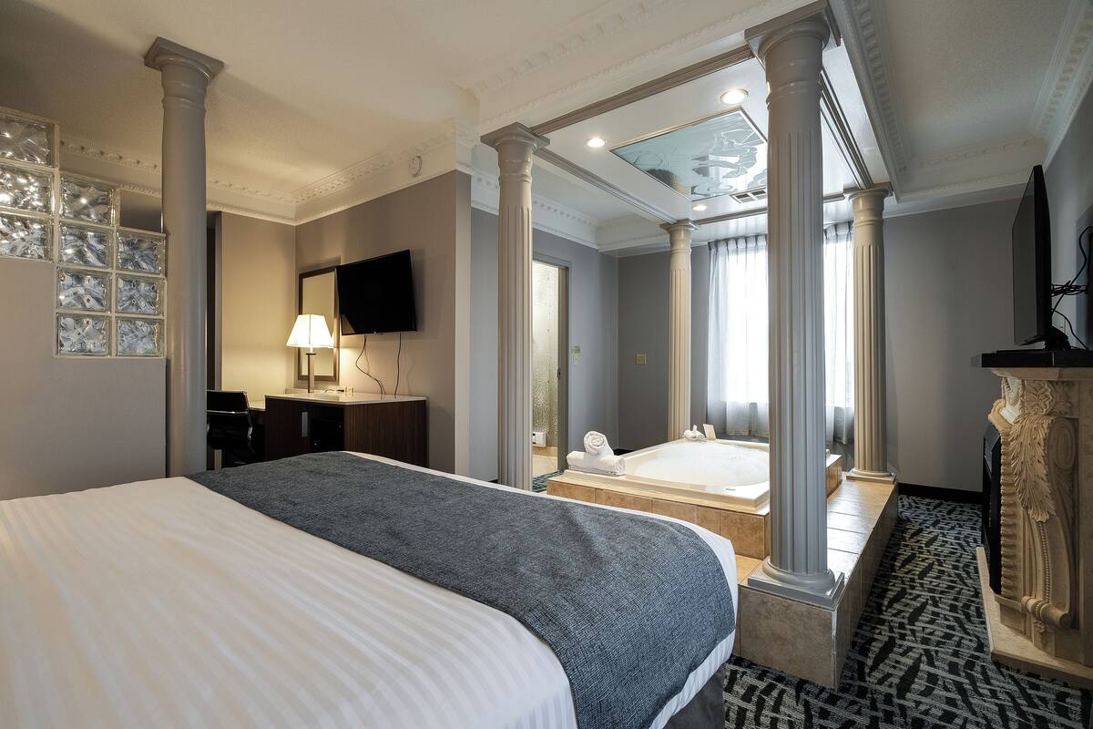 A hotel room with a large bed, a bathroom with a bathtub, and a TV mounted on the wall.