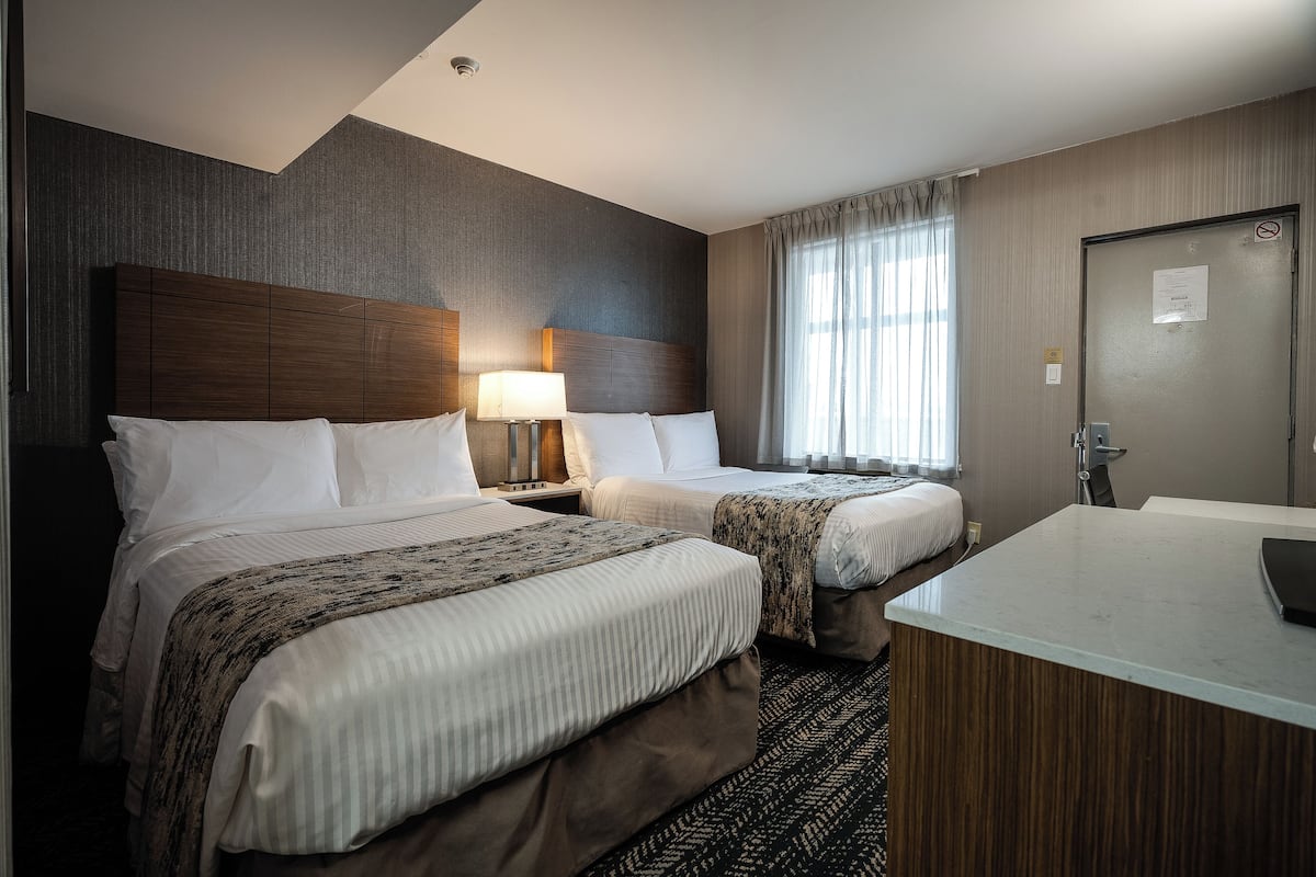 A hotel room with two beds, a large mirror, a desk, and a bathroom.