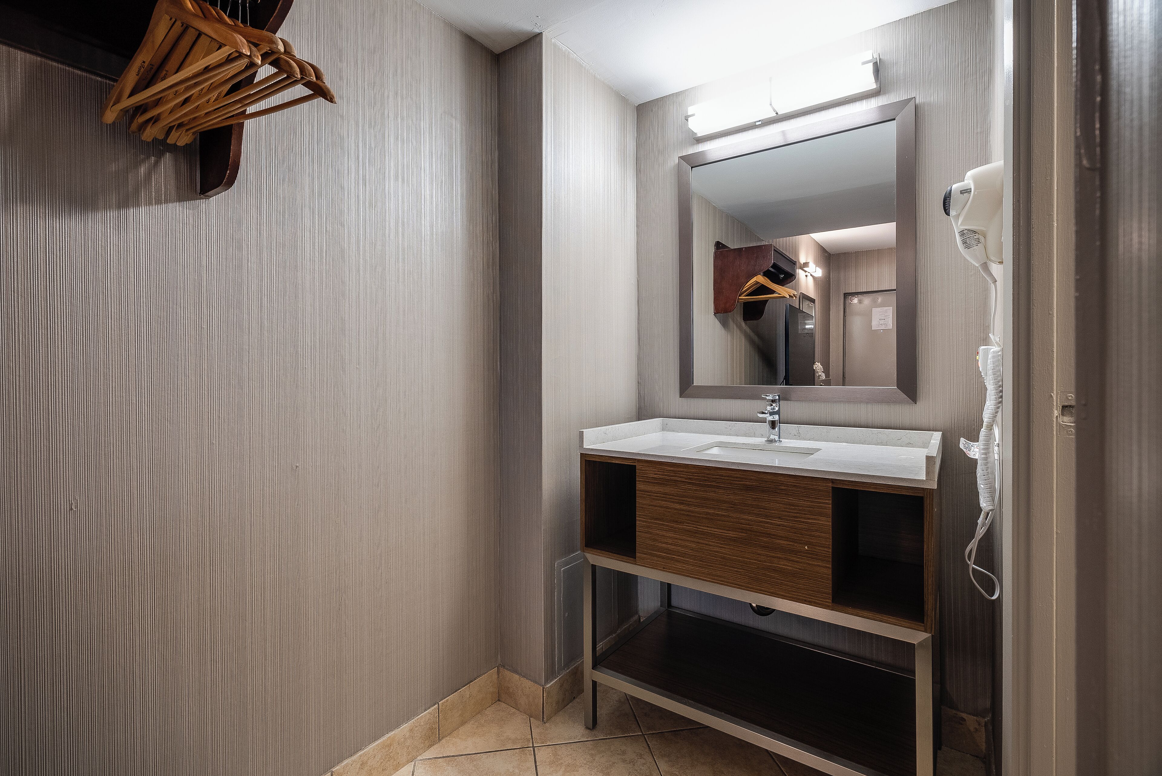 Un baño moderno con tocador de madera, un espejo grande y un secador de pelo en la pared.