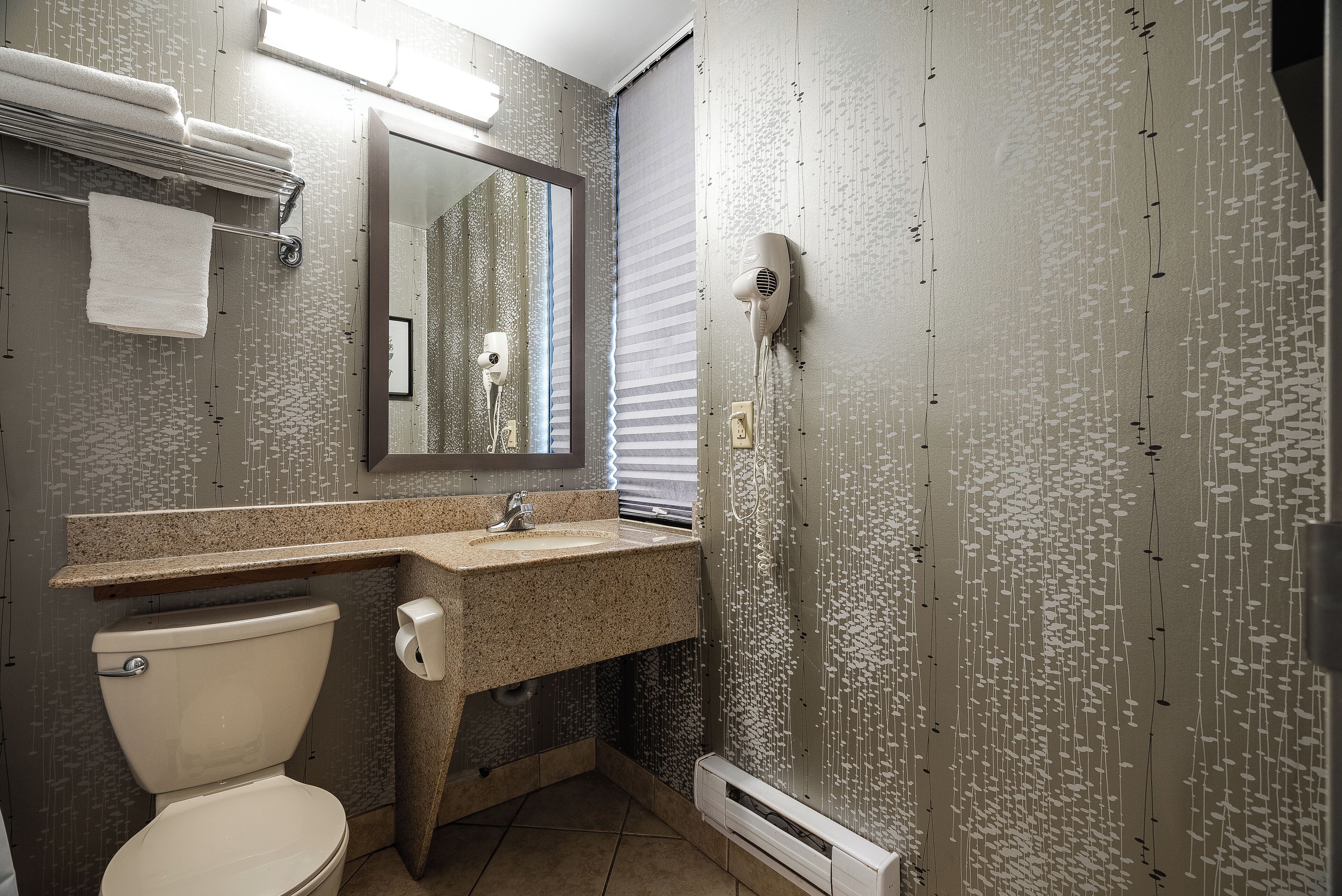 A bathroom with a toilet, sink, mirror, towel rack, and a hairdryer mounted on the wall.