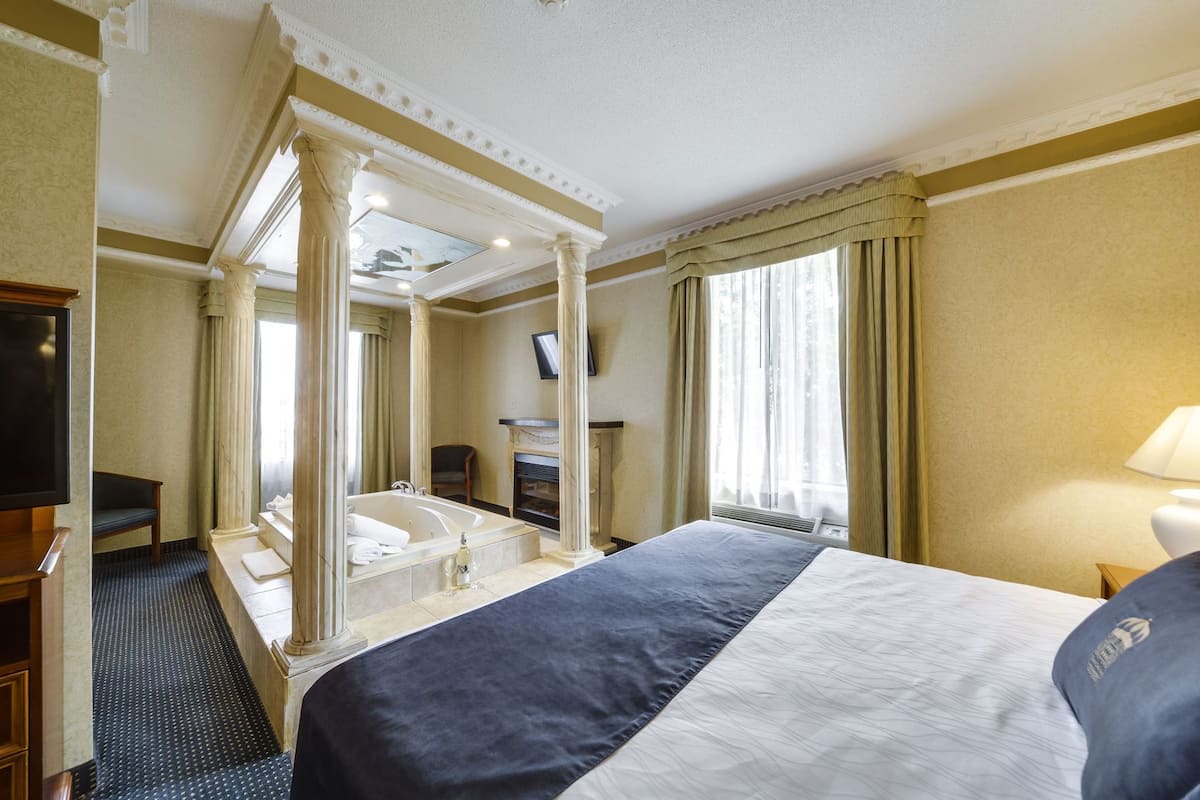 A hotel room with a large bed, a television, a fireplace, and a view of the outdoors.