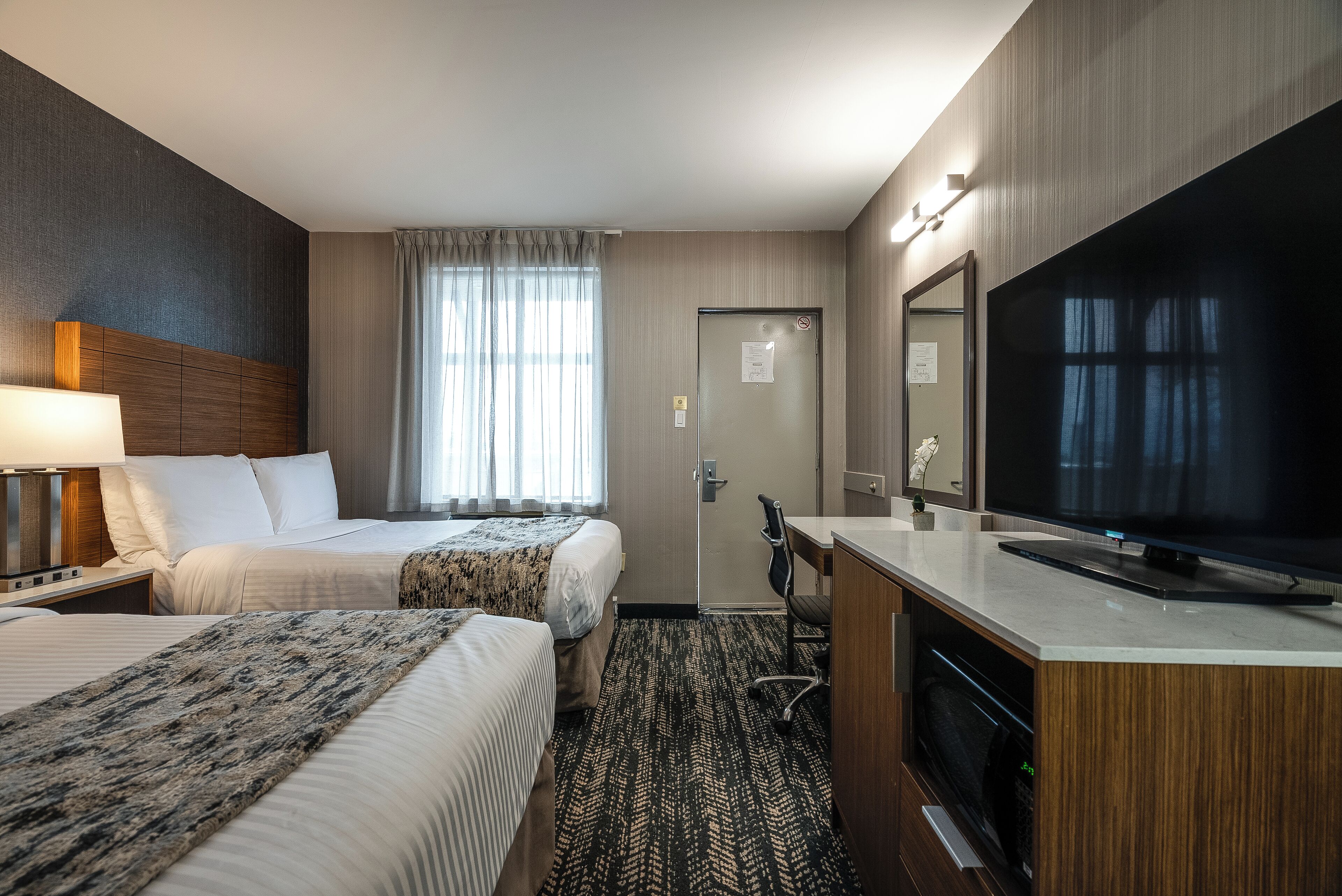 Een hotelkamer met twee bedden, een bureau, een televisie en een badkamers deur.