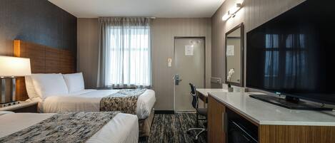 Een hotelkamer met twee bedden, een bureau, een televisie en een badkamers deur.