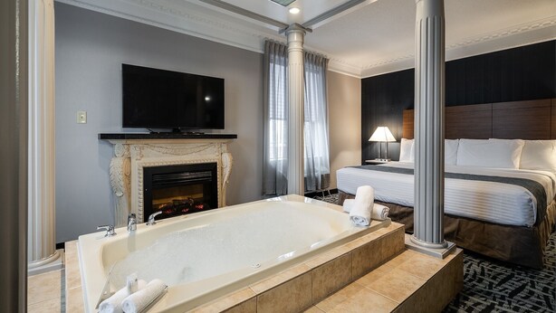 A modern hotel room with a large bathtub, a television, a bed, and a fireplace. - Monte Carlo Inn Toronto West Suites (Mississauga)