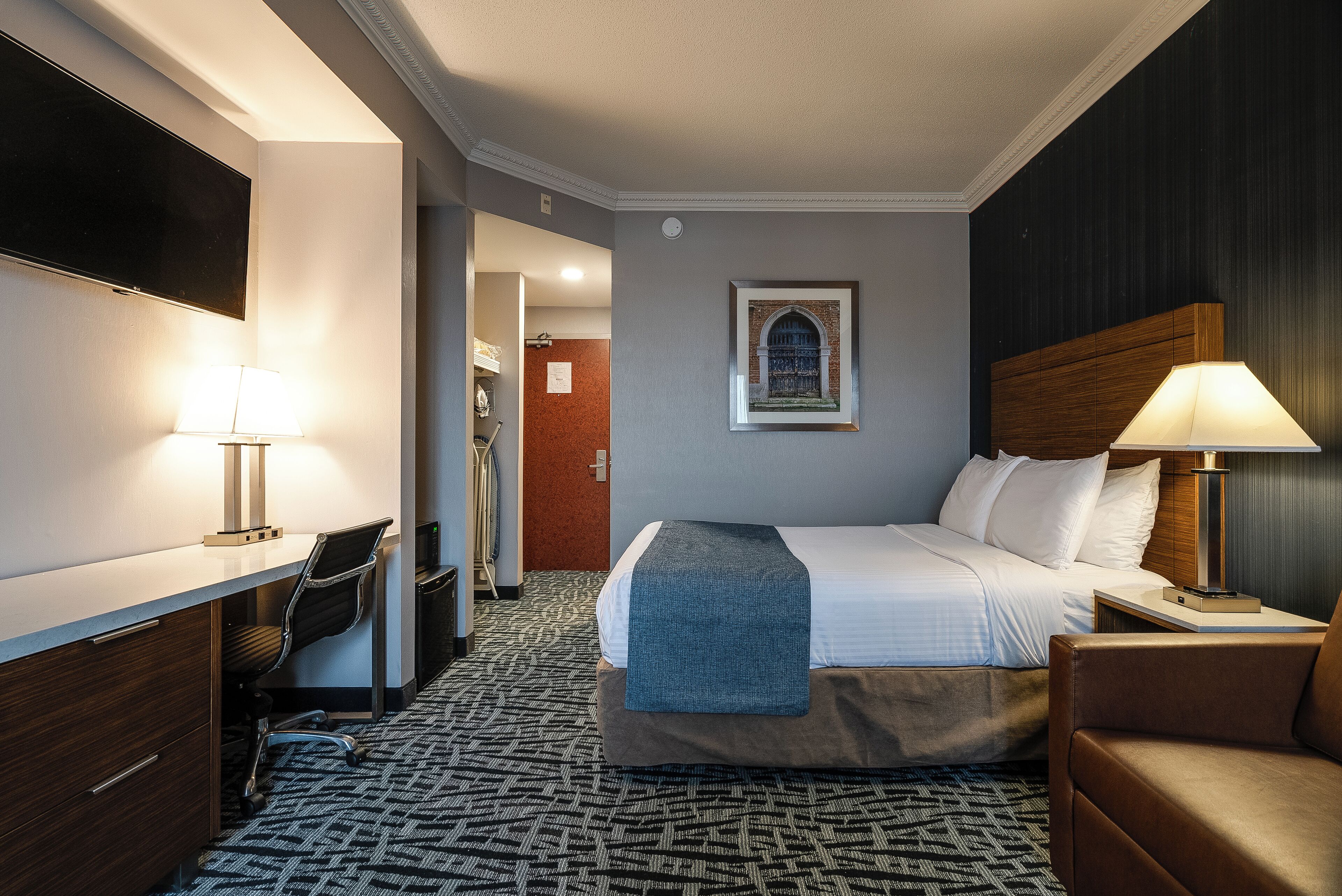 A hotel room with a bed, desk, chair, and a TV.