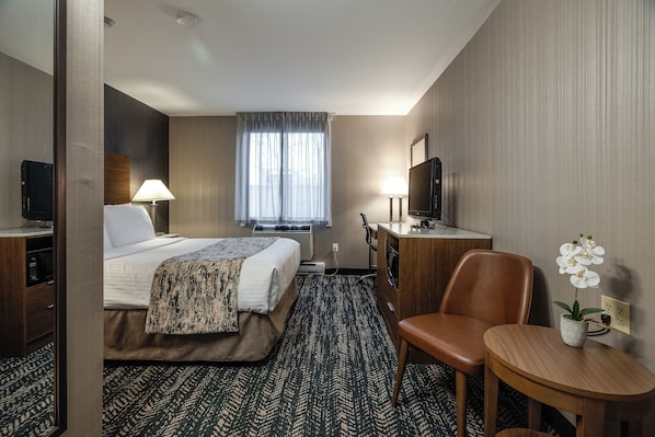 Une chambre d’hôtel équipée d’un lit, d’un bureau, d’une chaise, d’une télévision et d’une petite table sur laquelle est posée une plante.