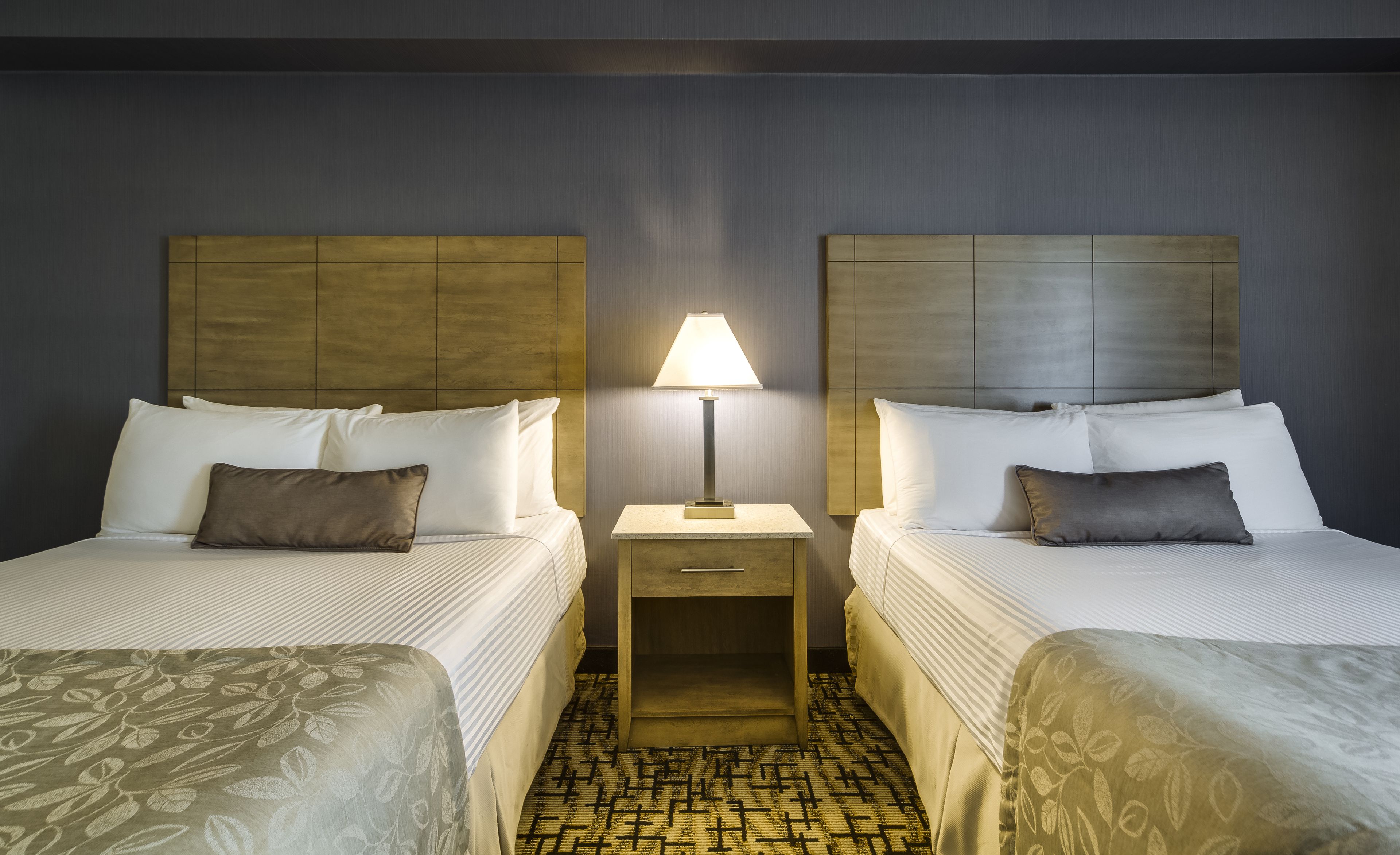 A hotel room with two beds, a nightstand with a lamp, and a patterned carpet.