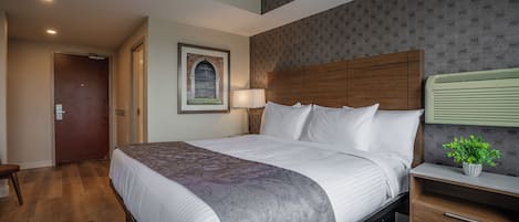 A hotel room with a large bed, a wooden nightstand, a bedside lamp, and a framed picture on the wall.